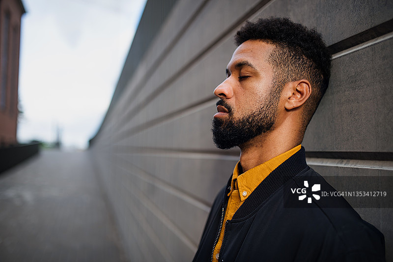 疲惫的年轻混血男子闭着眼睛靠在墙上图片素材