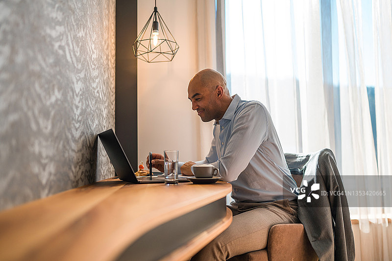 在酒店房间用笔记本电脑工作的混血商人图片素材