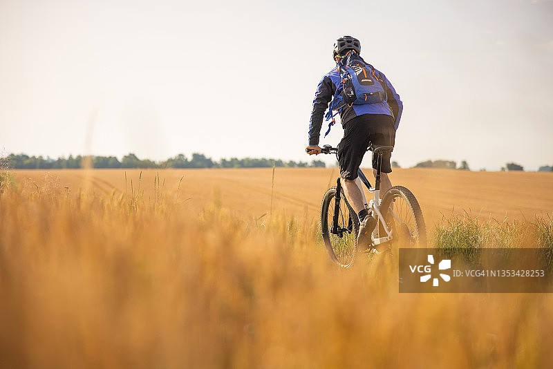 山地自行车手在乡村田野上骑行的背影图片素材