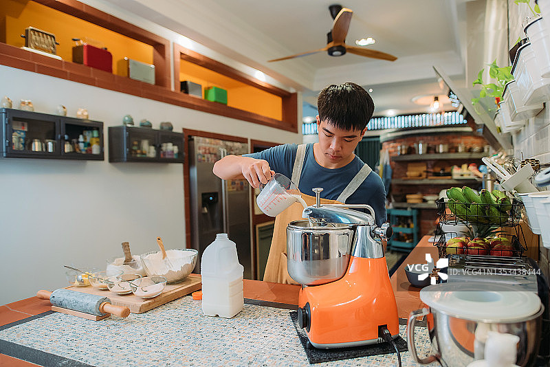 亚洲华裔青少年面包师将牛奶倒入厨房的面包搅拌机图片素材