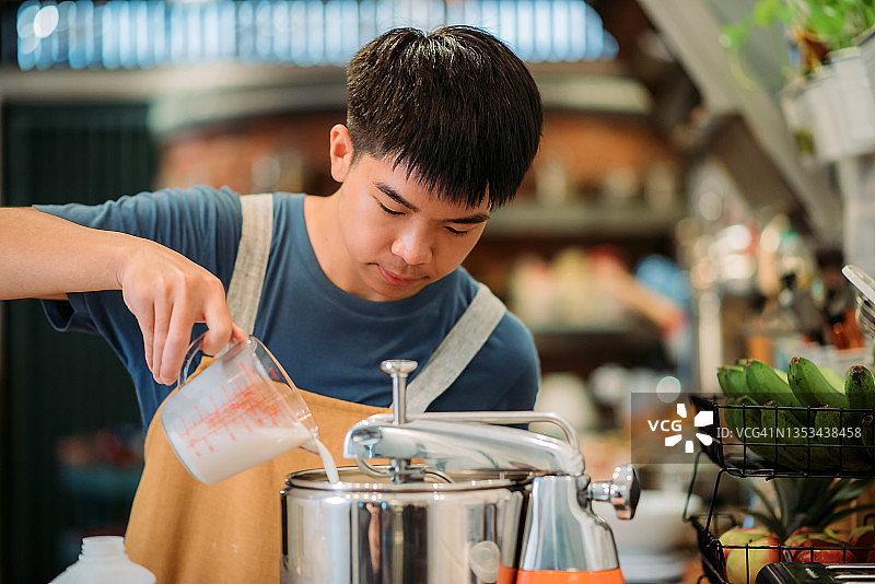 亚洲华裔青少年面包师将牛奶倒入厨房的面包搅拌机图片素材
