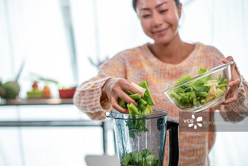 年轻女孩在厨房用搅拌机制作新鲜蔬果绿色排毒鸡尾酒图片素材