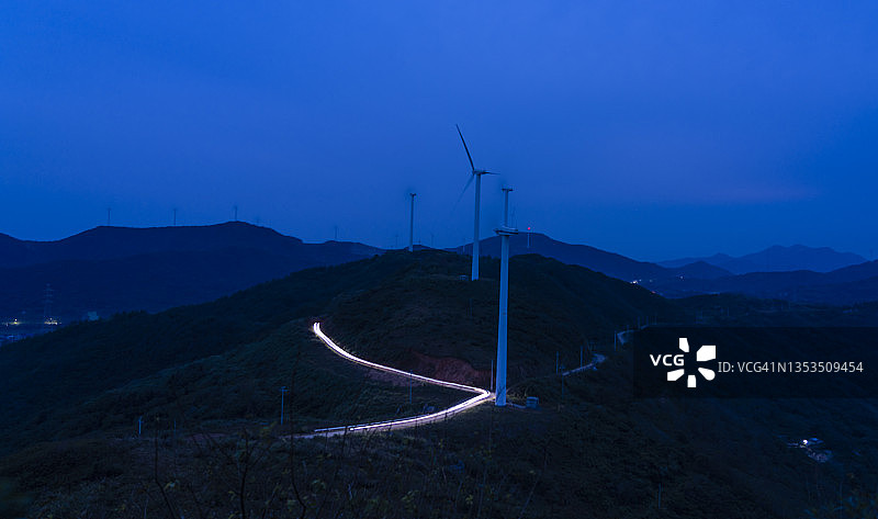 风力涡轮机、灯光和车辆在弯曲的山路上行驶的轨迹图片素材