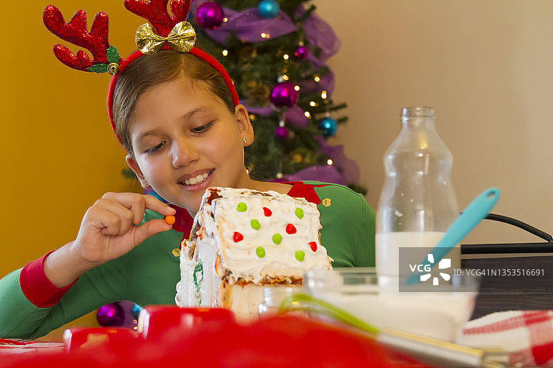 在拉丁美洲的家中，穿着圣诞衬衫的拉丁裔年轻女孩在圣诞夜烹饪和组装姜饼圣诞饼干屋的特写肖像图片素材