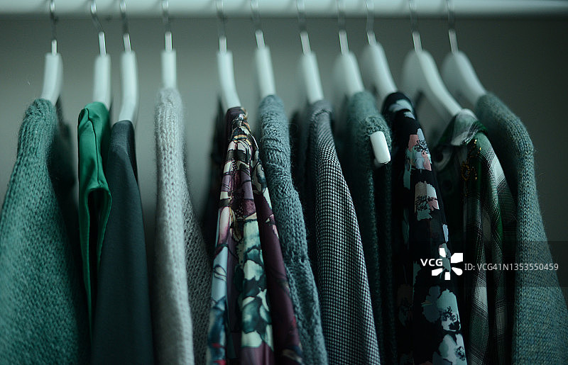 绿色色调的衬衫和针织毛衣挂在衣架上，按颜色协调排列图片素材