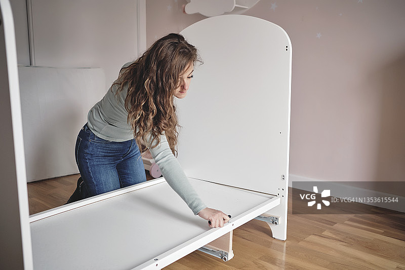 年轻母亲拆卸婴儿床，准备更换成床图片素材