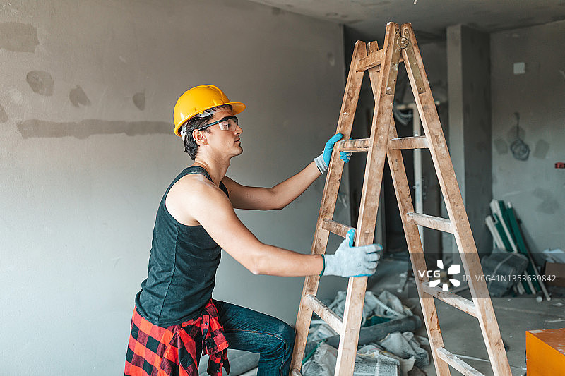 电工爬上梯子进行房屋翻新。建筑工人在安全帽中，使用梯子检查天花板上的电线图片素材