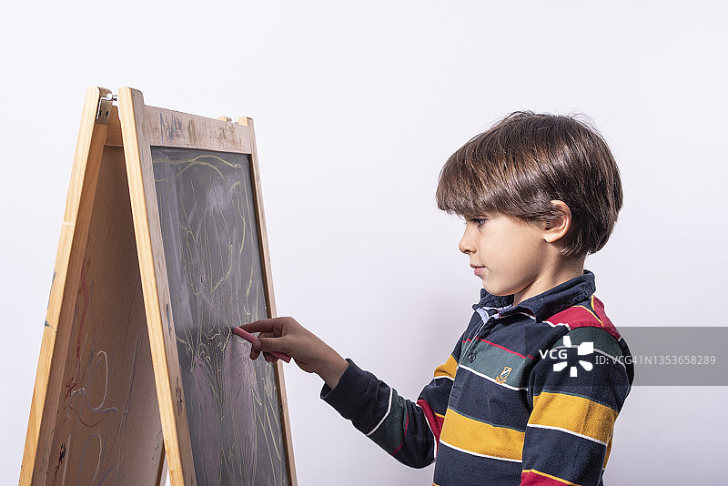 男孩在工作室背景的黑板上绘画图片素材