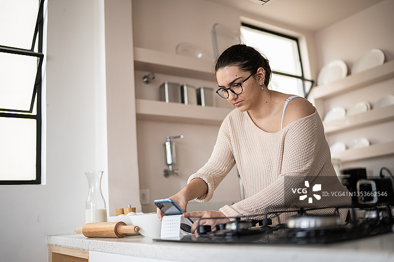 年轻女人在家看手机菜谱做饭图片素材