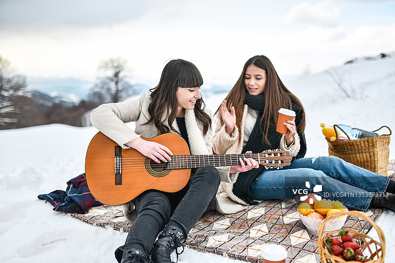 笑容满面的女性在雪地野餐时弹吉他喝咖啡图片素材