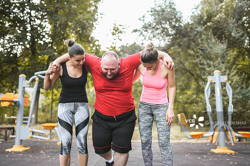 训练后女性朋友帮助移动的疲惫超重男人图片素材