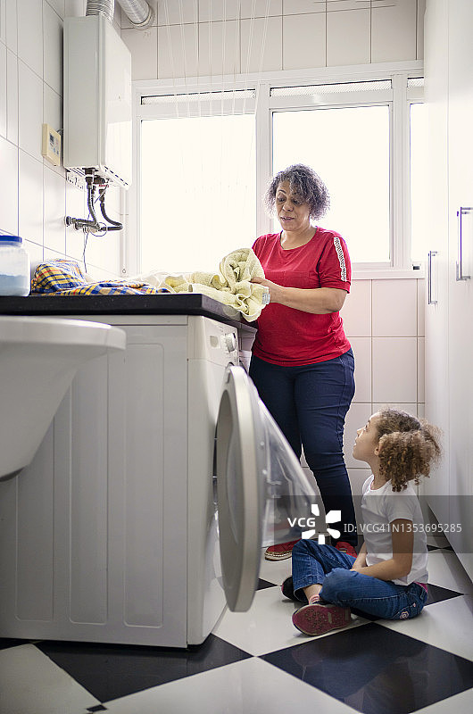 祖母和孙女在洗衣房里把脏衣服放进洗衣机图片素材