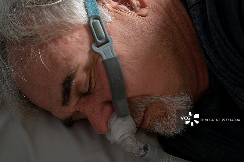 被诊断出患有睡眠呼吸暂停后使用CPAP机的中年男人图片素材