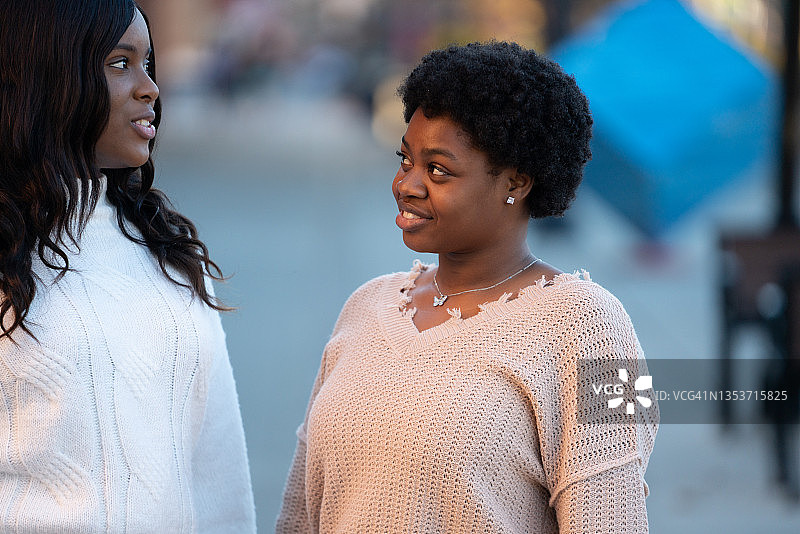 两名20多岁的非裔美国海地女孩在繁华的零售街道上交谈图片素材