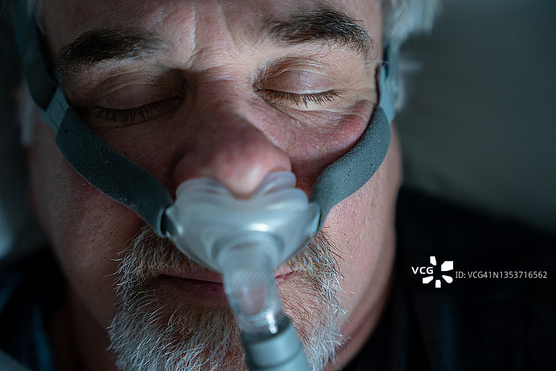 被诊断出患有睡眠呼吸暂停后使用CPAP机的中年男人图片素材