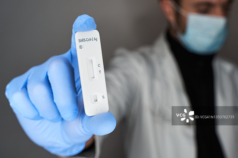 医生戴着蓝色一次性手套和防护口罩，手持新冠病毒检测工具图片素材