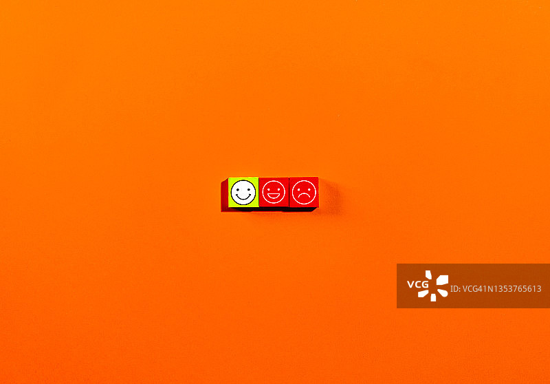 客户服务体验和满意度调查概念，面部表情呈负面、中性和正面，位于桌子上的木制立方体上，橙色背景图片素材