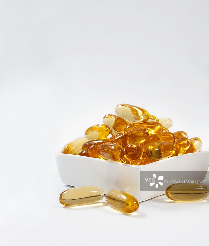 白色背景下瓷碗里的鱼油胶囊图片素材