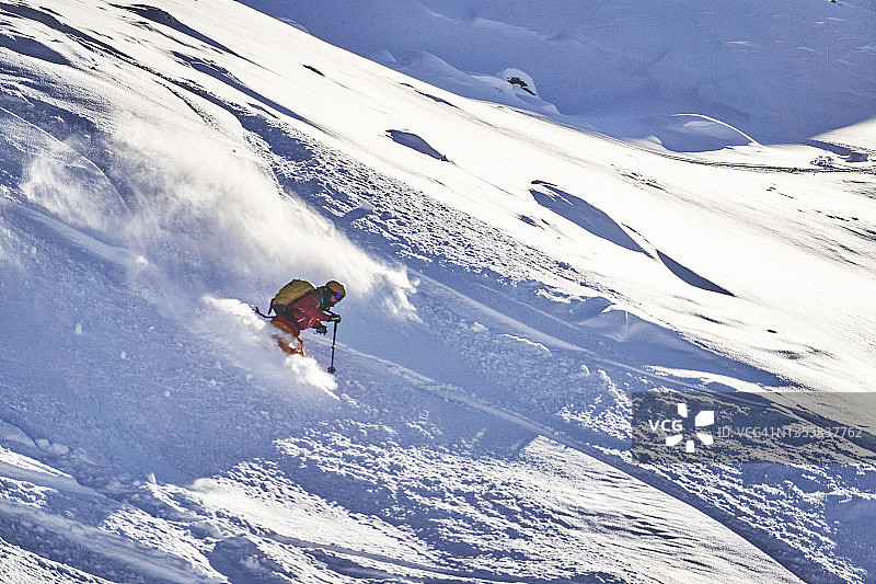 阳光下，滑雪者沿雪山山脊滑下图片素材