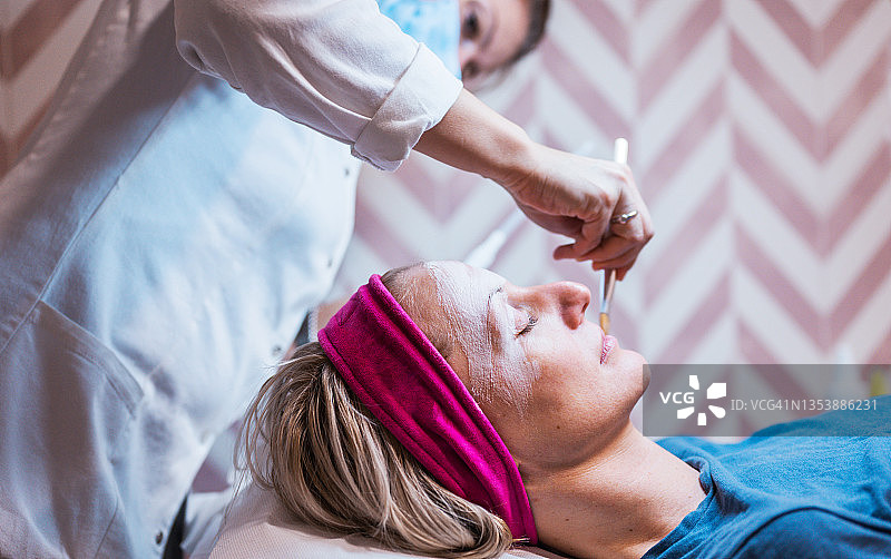 在水疗床上闭着眼睛接受面部泡沫按摩以去除死皮的女人图片素材