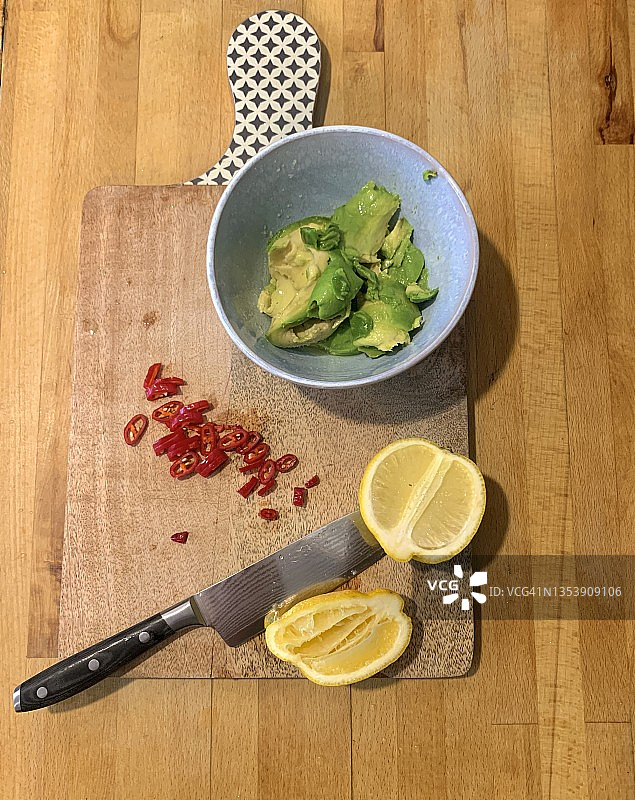 农舍厨房台面上的木制砧板，配有半个柠檬、锋利的大刀、切碎的红辣椒和鳄梨碗，用于制作纯素蘸酱的食材，2021年11月在墨西哥城准备健康美味的纯素墨西哥食物图片素材