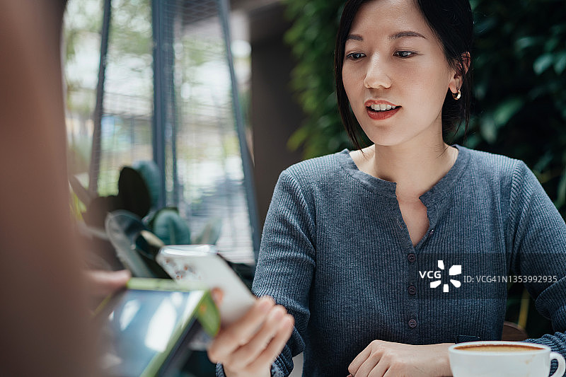 亚洲年轻女性在餐厅用手机进行移动支付特写图片素材