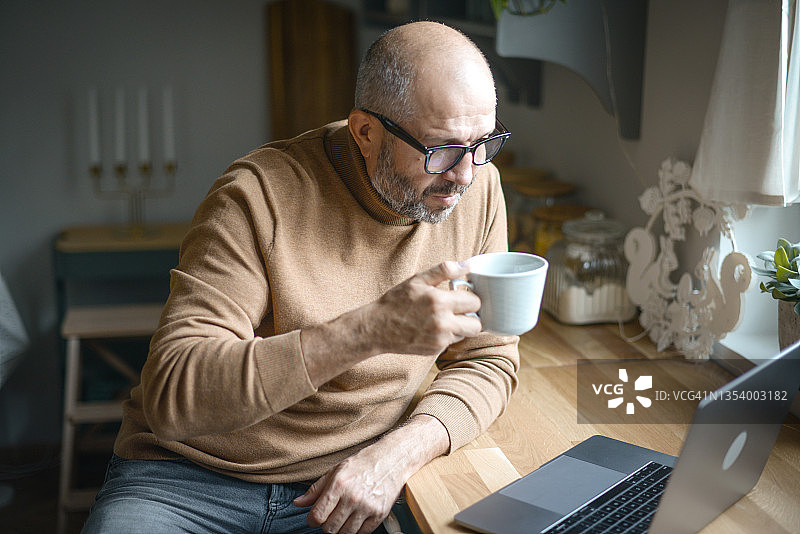 在舒适的家庭厨房里的年长的成年男子（笔记本电脑，视频会议）图片素材