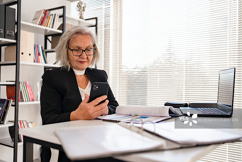 在工作中用智能手机交谈的年长女商人图片素材