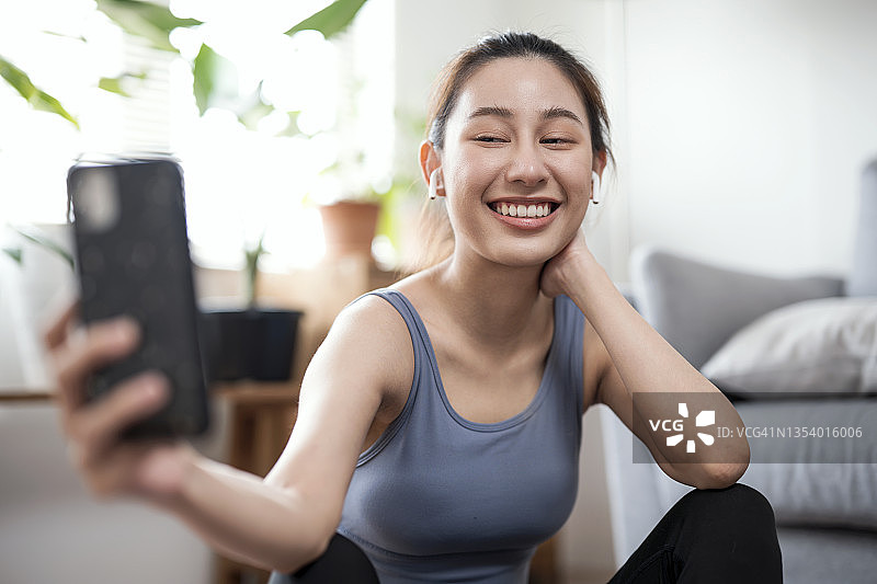 健康的亚洲年轻女人在公寓锻炼后与瑜伽社区休息时用手机自拍或进行视频通话图片素材