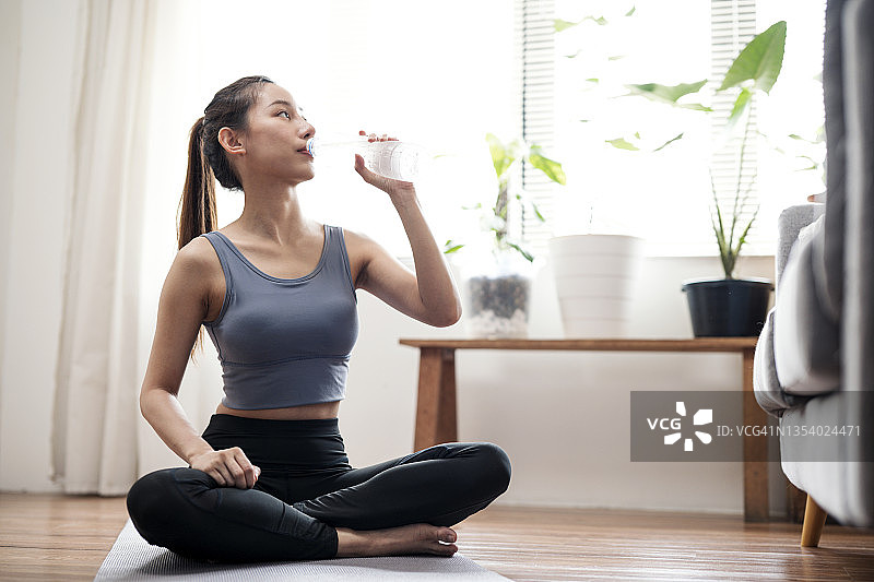 运动后饮水有助于维持血压，年轻女人在公寓锻炼或瑜伽后饮水图片素材