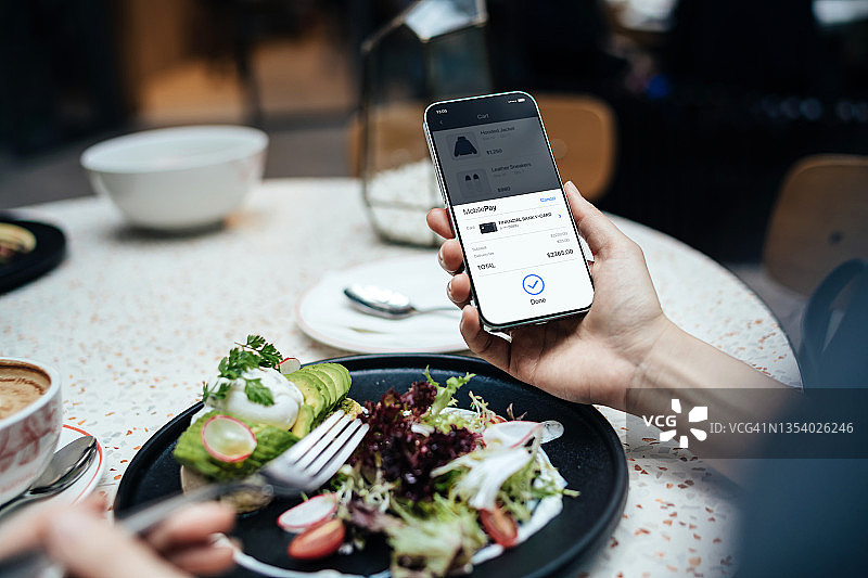 年轻女子在餐厅用餐时用手机网购并用信用卡支付的肩上视角图片素材