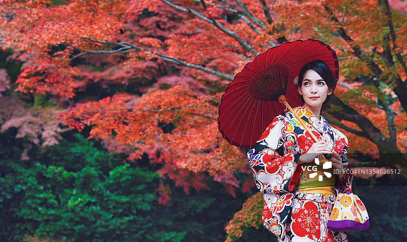 亚洲女人在秋天的公园里穿着日本传统和服。在秋天，年轻女人在日本花园里穿着传统的日本和服，周围是色彩鲜艳的枫树。日本京都。图片素材