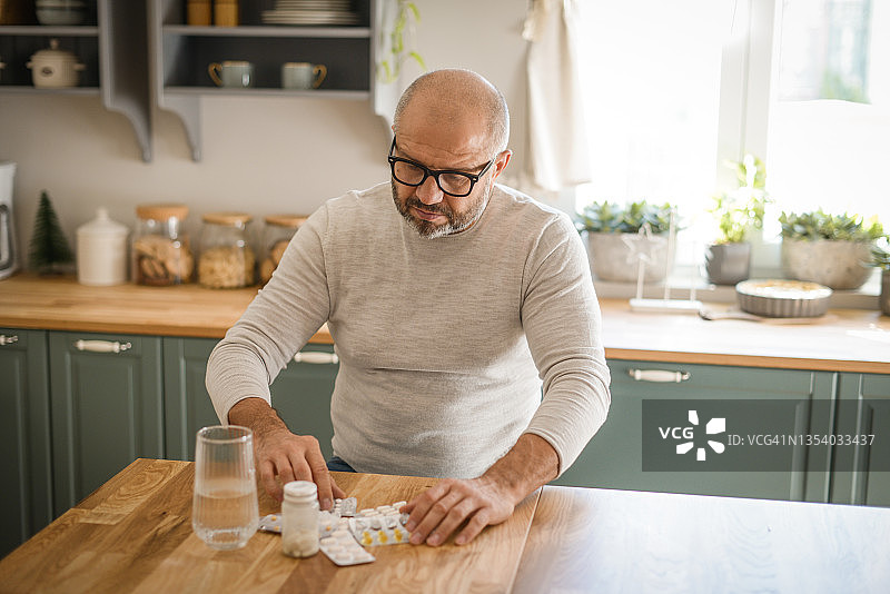 在舒适的家庭厨房里的中年男人（正在服药）图片素材