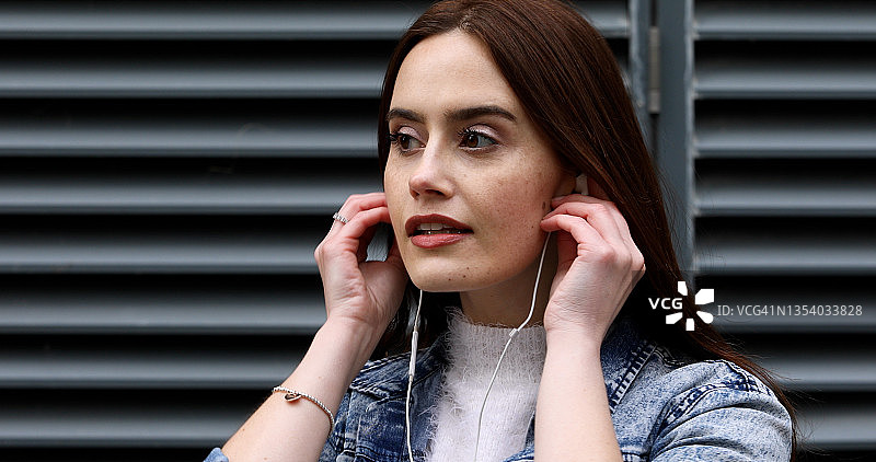 年轻女人戴耳机站在建筑金属格栅前图片素材