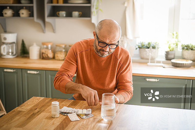 在舒适的家庭厨房里的中年男人（正在服药）图片素材