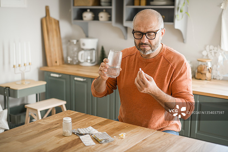 在舒适的家庭厨房里的中年男人（正在服药）图片素材