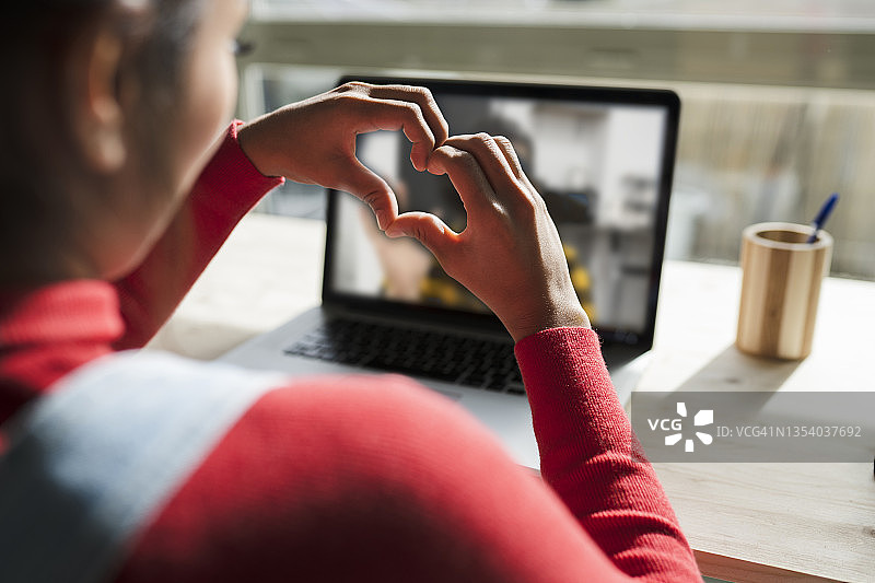 女人在电脑前视频通话手比心形图片素材
