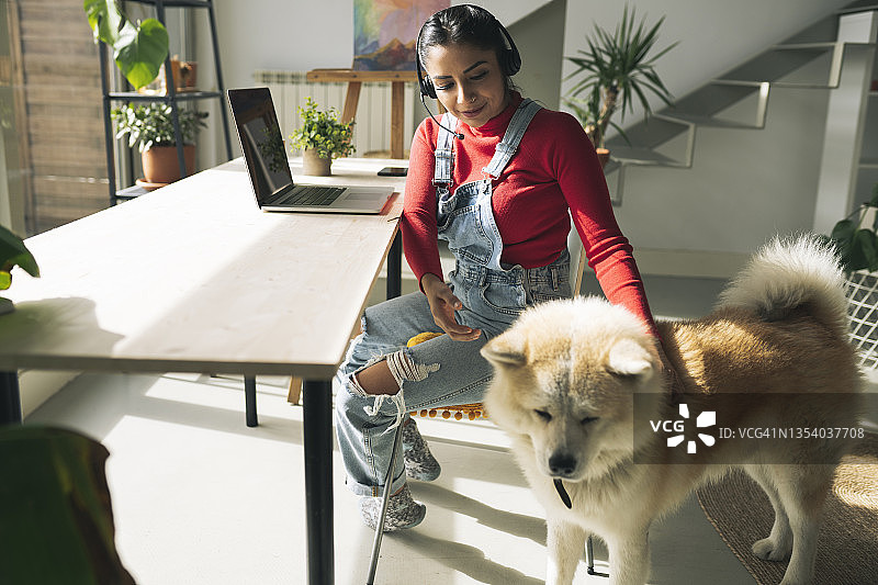 在家办公时与宠物一起坐在客厅桌旁的西班牙裔拉丁裔女性图片素材