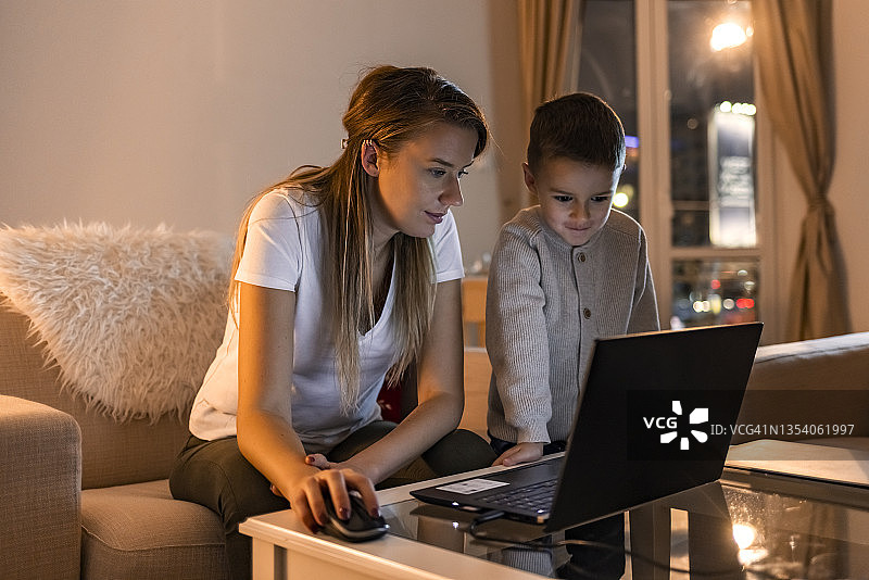 母亲在家里用笔记本电脑监督儿子在线学习图片素材
