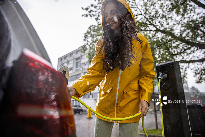 年轻女子在雨中将电插头插入汽车图片素材