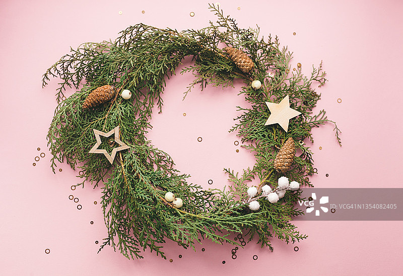 用天然松枝、装饰品和浆果制成的粉红色背景上的常青圣诞花环，家居装饰DIY创意图片素材