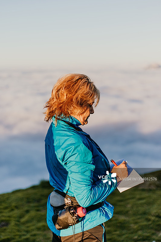 中年女徒步旅行者在山顶的书上写作图片素材