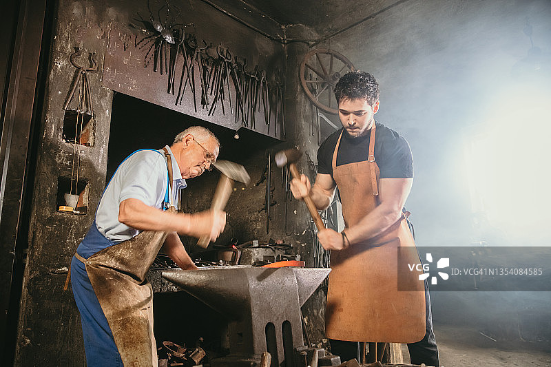 两位铁匠用锤子敲打炽热的金属图片素材