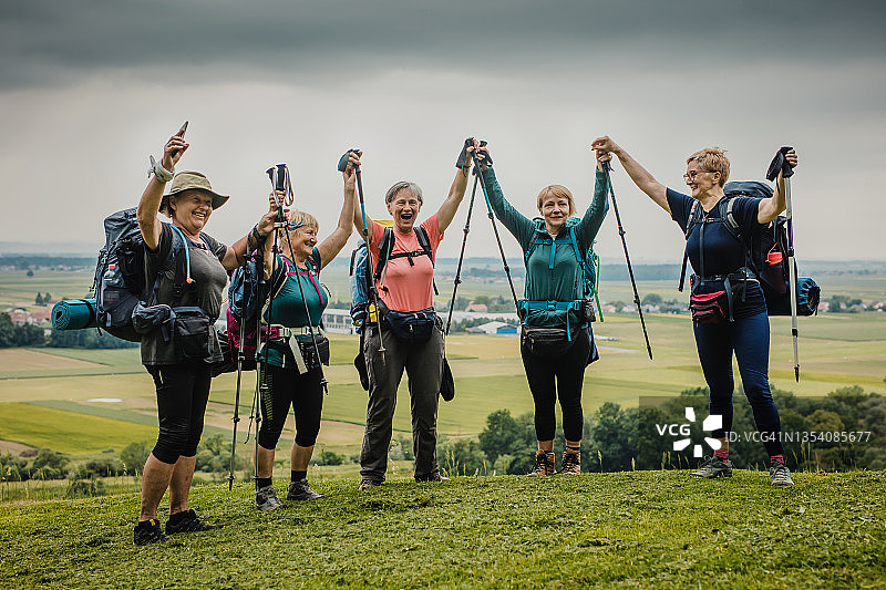 微笑的中年女徒步者在山丘上举起双臂图片素材