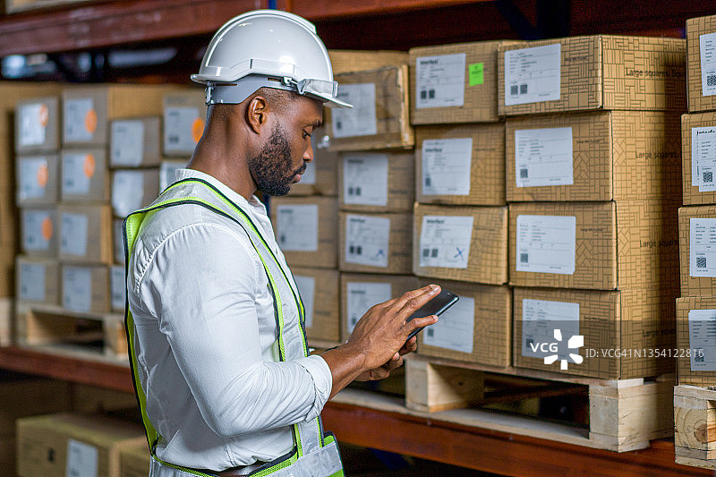 英俊的仓库工人使用数字平板电脑检查库存，货架上放着纸板箱图片素材