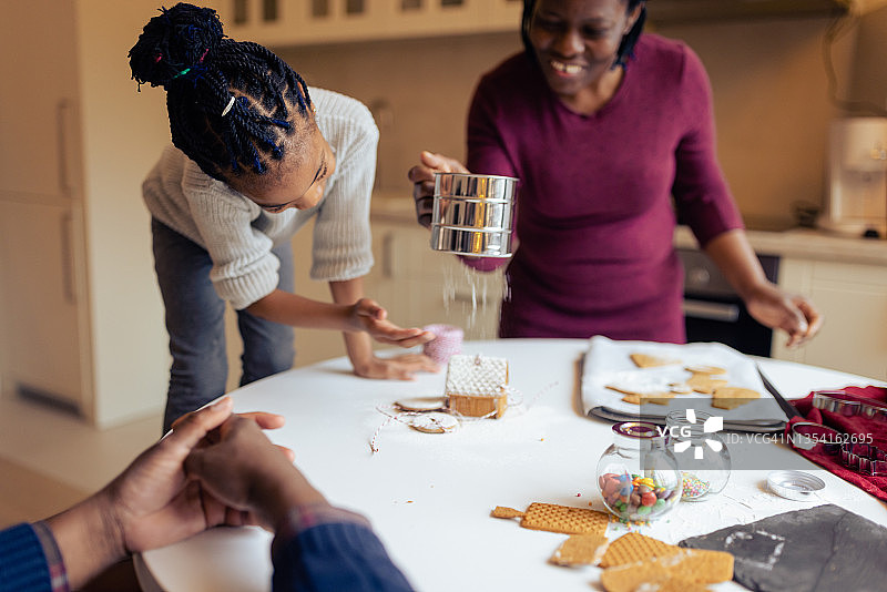 小女孩和妈妈、爷爷一起制作圣诞姜饼屋图片素材