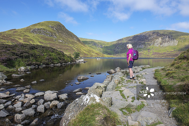 在苏格兰莫法特附近Grey Mare’s Tail瀑布小道上徒步旅行的年长妇女停下来观看小道顶端的湖泊图片素材