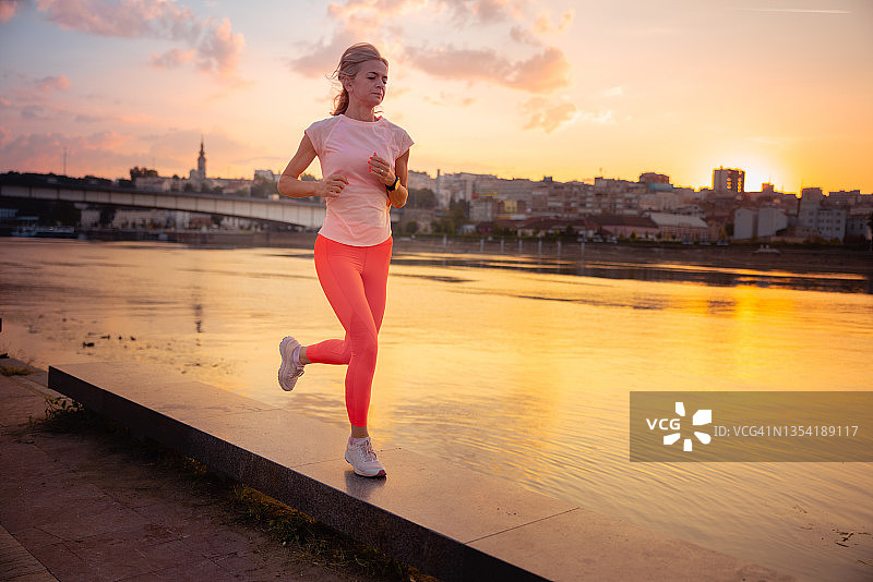 在城市黎明时分，活跃的女性在河边平台上跑步图片素材
