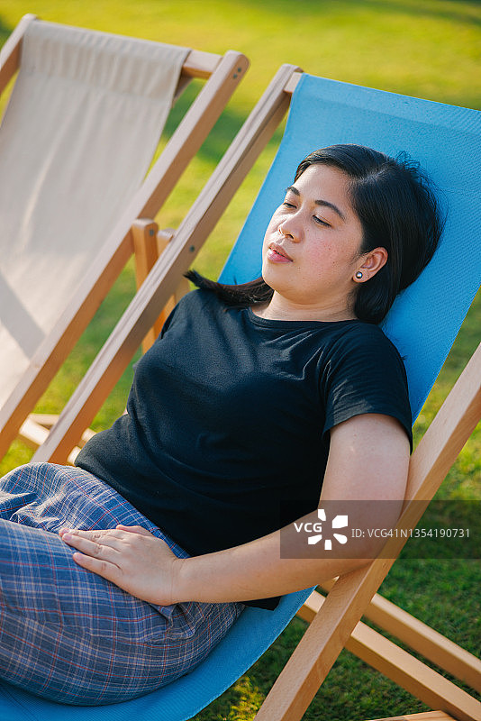 在木制躺椅上闭着眼睛放松的女人图片素材