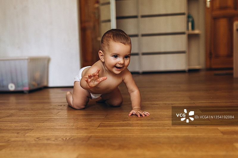 穿着尿布在家在地板上爬行的小宝宝图片素材
